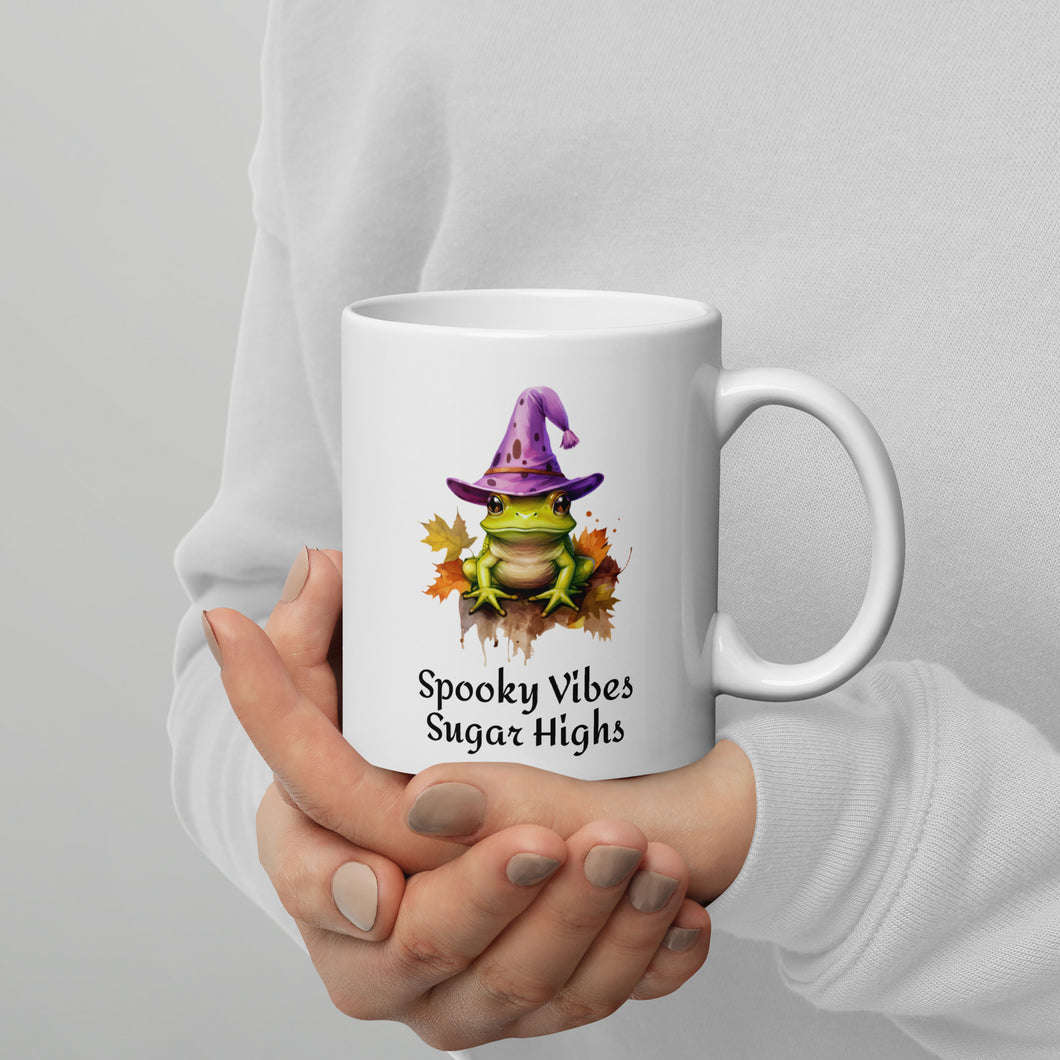 white mug with green frog on a bed of leaves and wearing a purple witch hat says spooky vibes sugar highs. Microwave and dishwasher safe