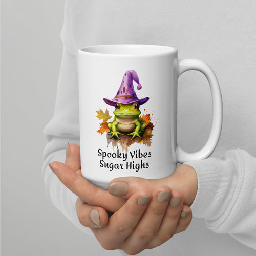 white mug with green frog on a bed of leaves and wearing a purple witch hat says spooky vibes sugar highs. Microwave and dishwasher safe